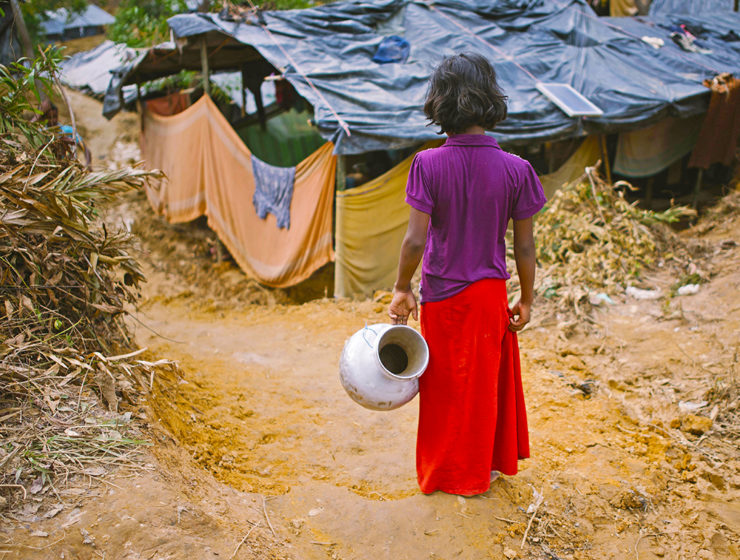 En rohingyaflicka i flyktinglägret Balukhali i Bangladesh går med ett metallkärl i handen för att hämta vatten.